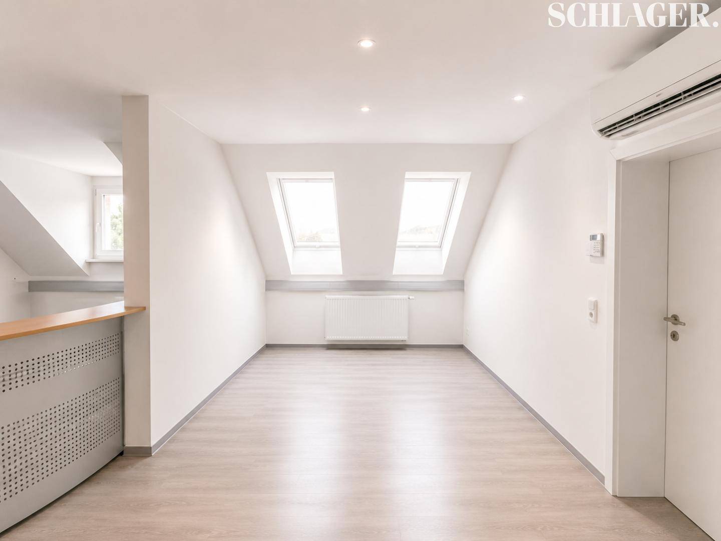 Heller Raum mit Laminatboden, zwei Dachfenstern und einer Klimaanlage, geeignet als Büro.