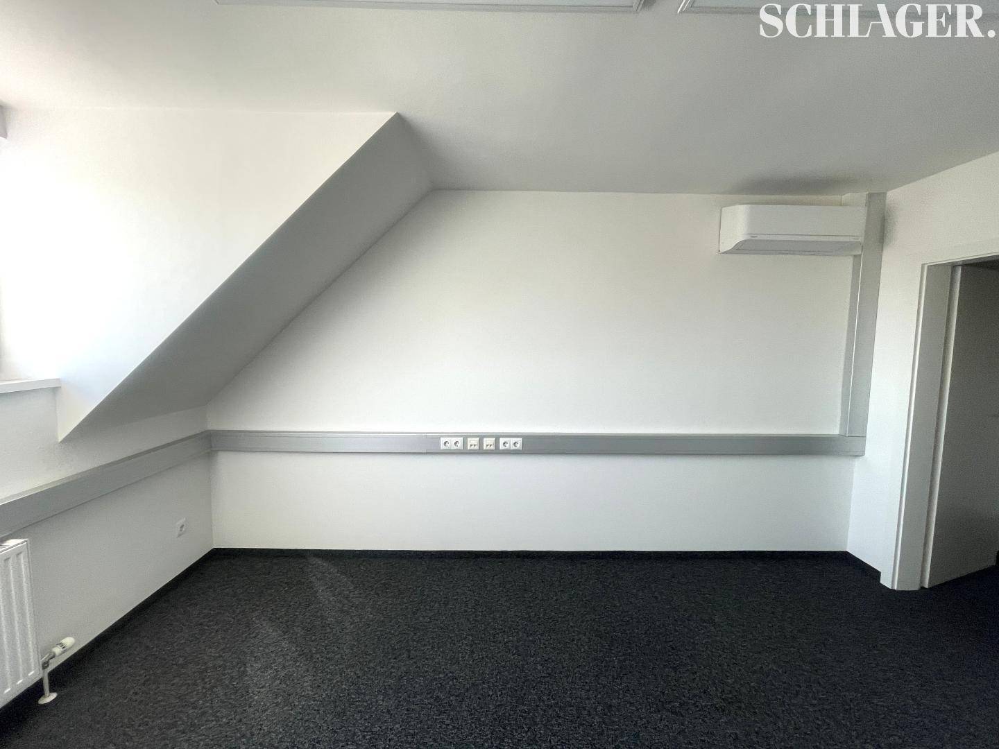 Geräumiger Büroraum im Dachgeschoss mit Teppichboden und Klimaanlage an der Wand.