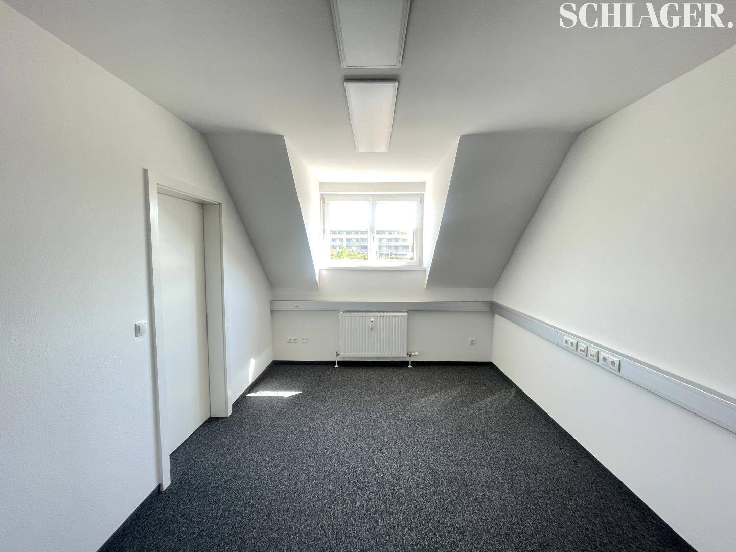 Helles Dachgeschossbüro mit Teppichboden, Dachfenster und schrägen Wänden.