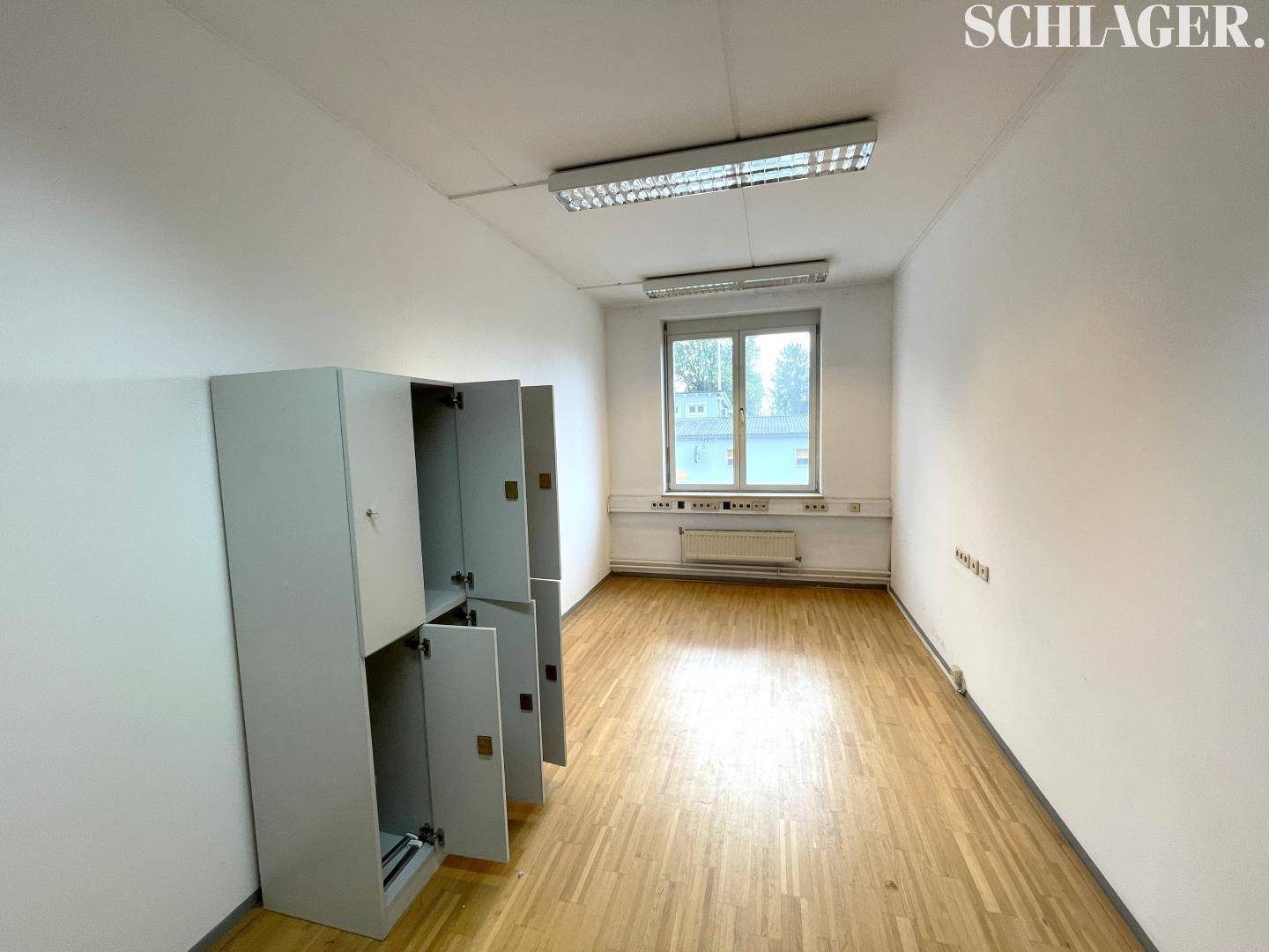 Geräumiger Büroraum mit Holzfußboden, Fenster und praktischen Spinden an der Wand.