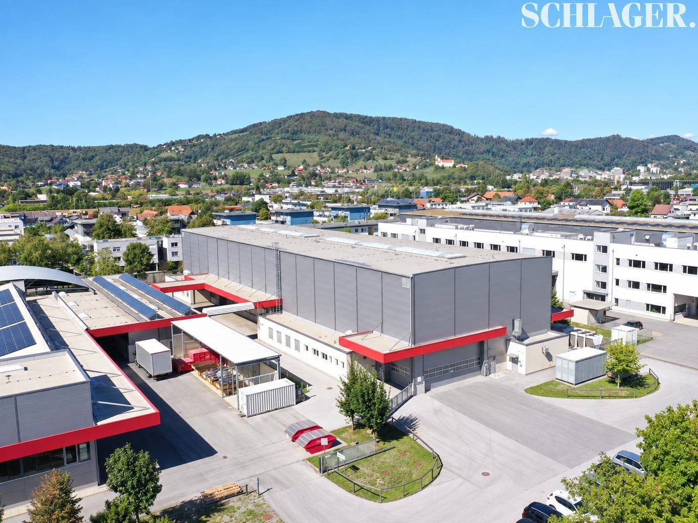 Übersichtliche Luftaufnahme des modernen Industriegebäudes mit angrenzenden Parkflächen und grüner Umgebung.