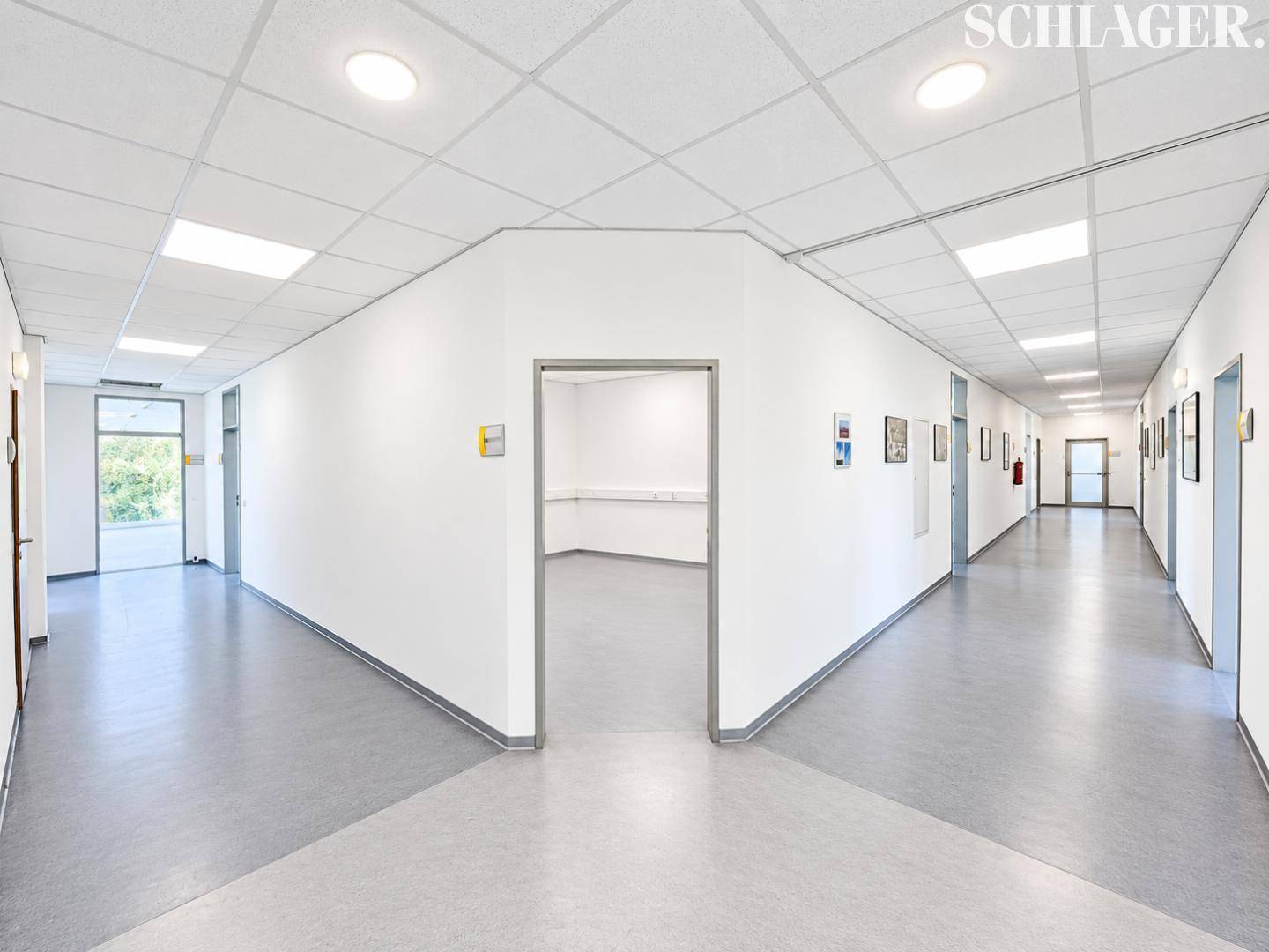 Langer, heller Flur mit mehreren Türen zu Büroräumen und einer modernen abgehängten Decke mit Einbauleuchten.