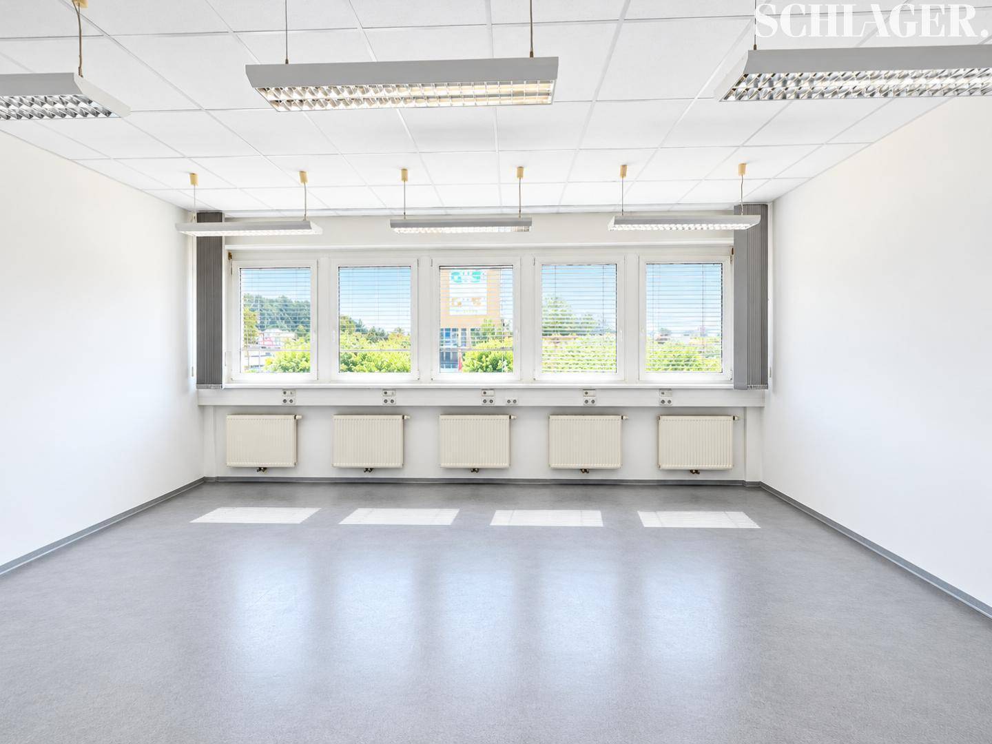 Heller, leerer Büroraum mit mehreren Fenstern, die viel Tageslicht hereinlassen, und einer abgehängten Decke.