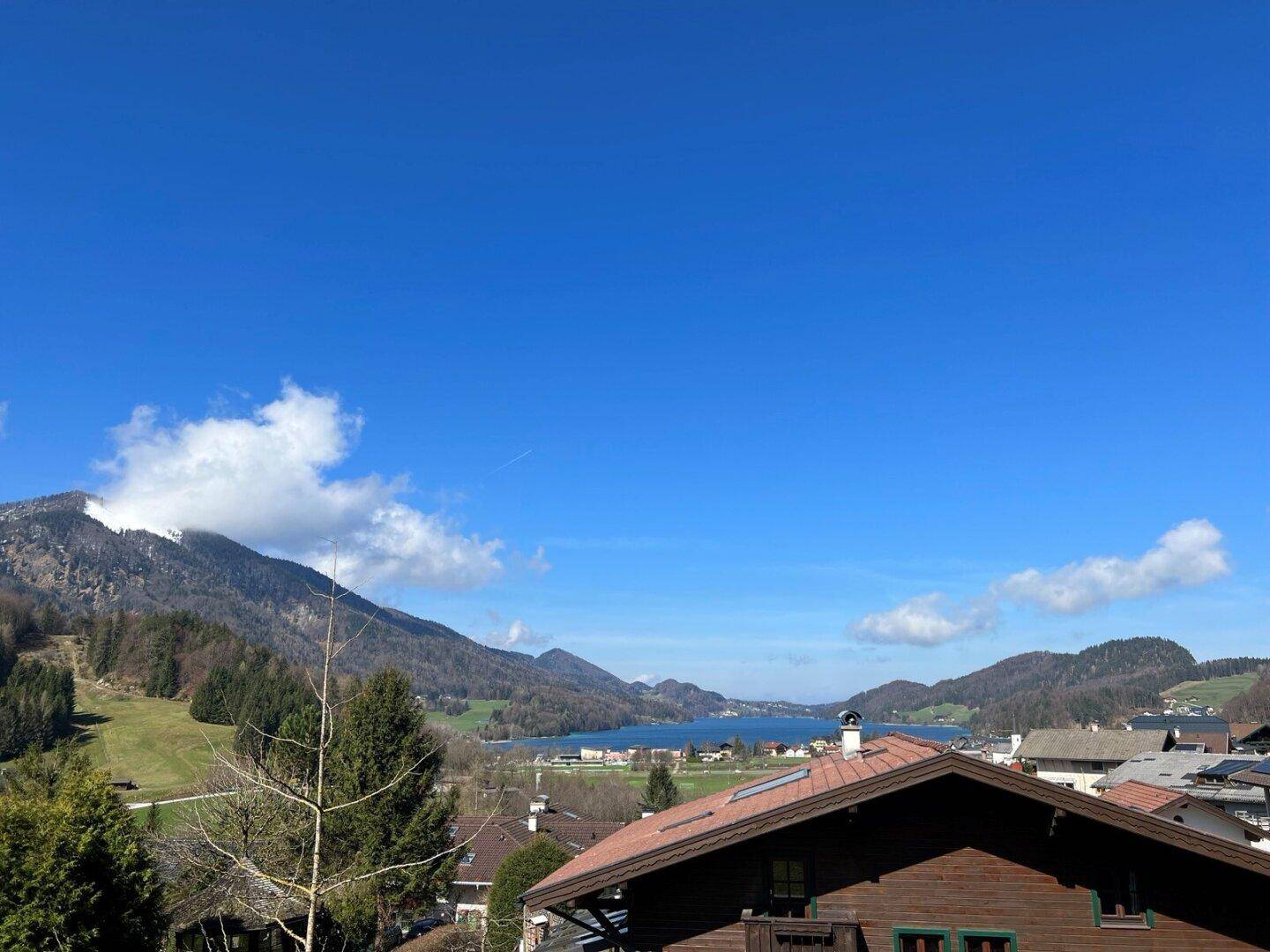 Panoramablick auf einen malerischen See und die umliegenden Berge unter strahlend blauem Himmel.