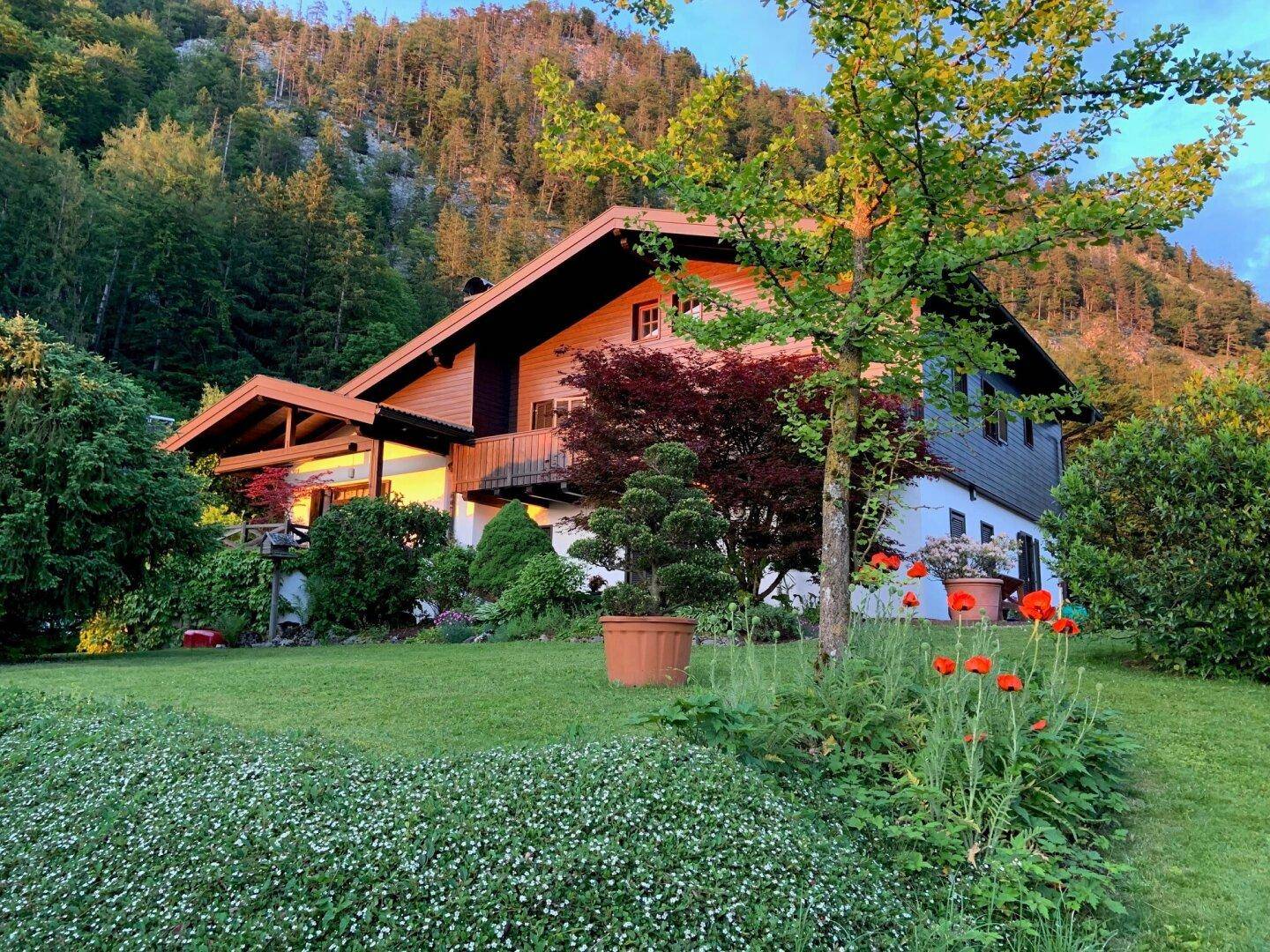 Charmantes Haus mit gepflegtem Garten und Bergblick, umgeben von üppiger Natur und Bäumen.
