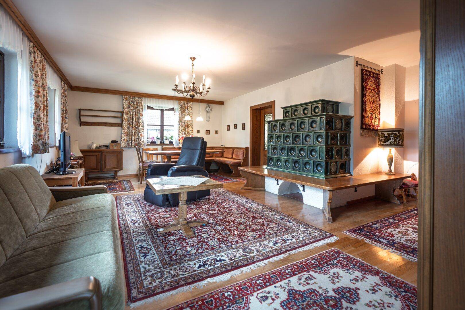 Gemütliches Wohnzimmer mit traditionellem Kachelofen, Holzboden und Teppichen.