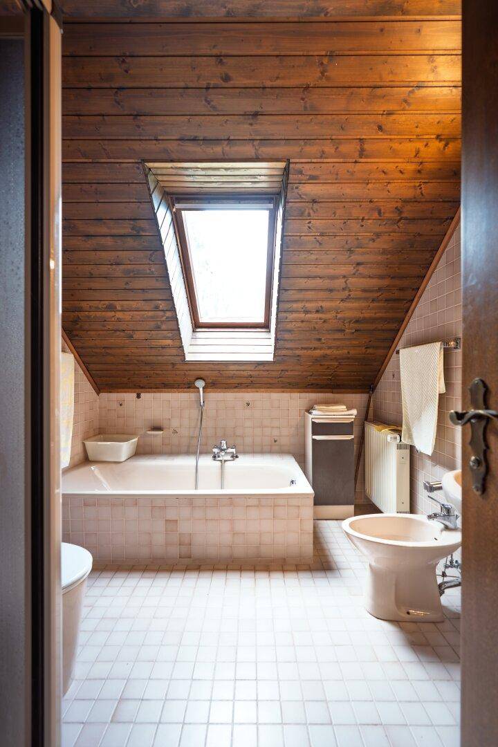 Badezimmer im Dachgeschoss mit Badewanne, Dachfenster und Holzverkleidung.