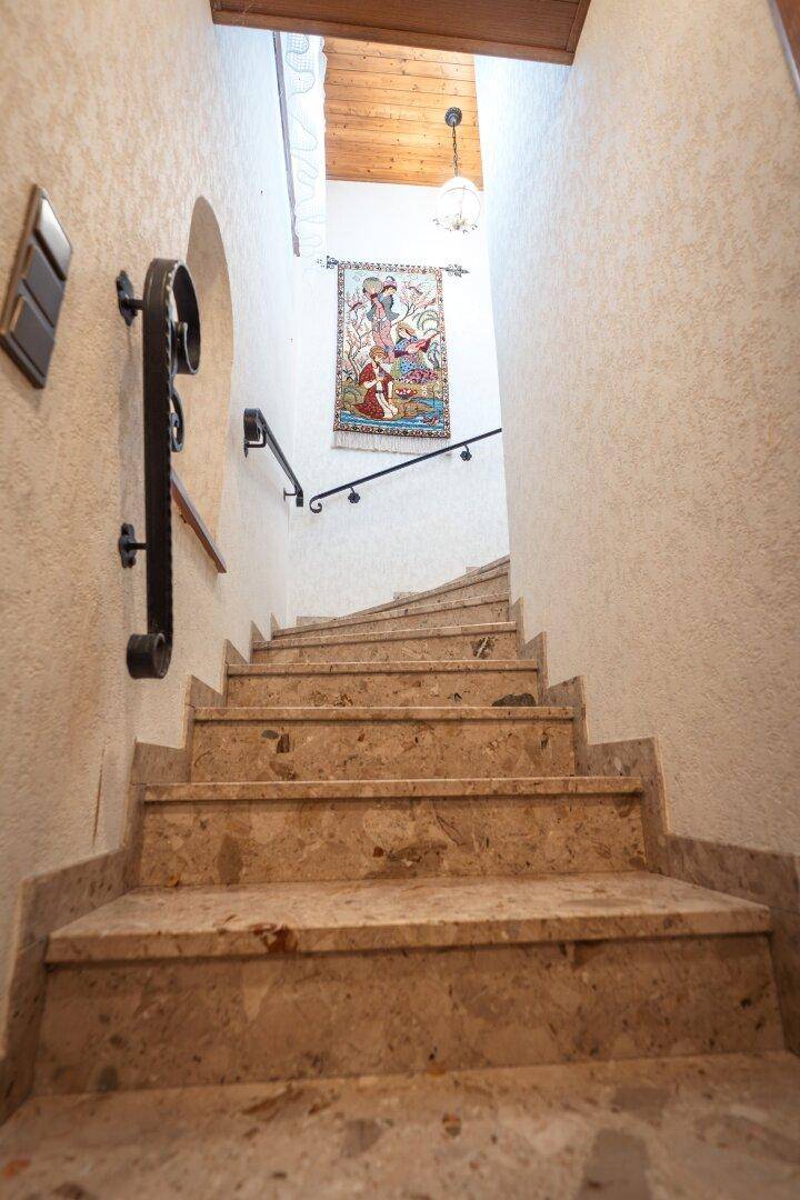 Treppenhaus mit Steinstufen, schmiedeeisernem Geländer und Wandteppich.