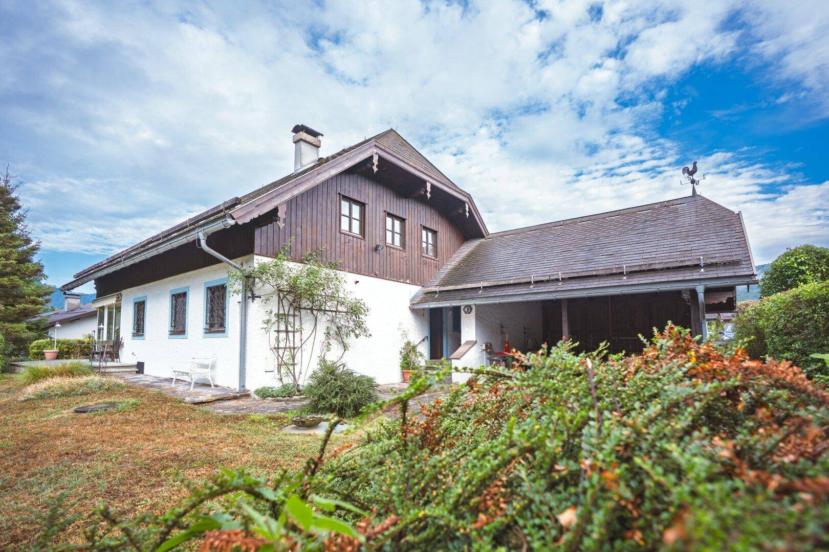 Seitenansicht des traditionellen Hauses mit weißer Fassade, Holzelementen und gepflegtem Gartenbereich.