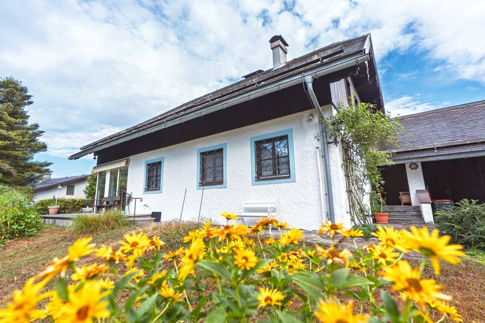 Vorderansicht des Hauses mit blühenden Blumen im Vorgarten und blauer Himmelskulisse.