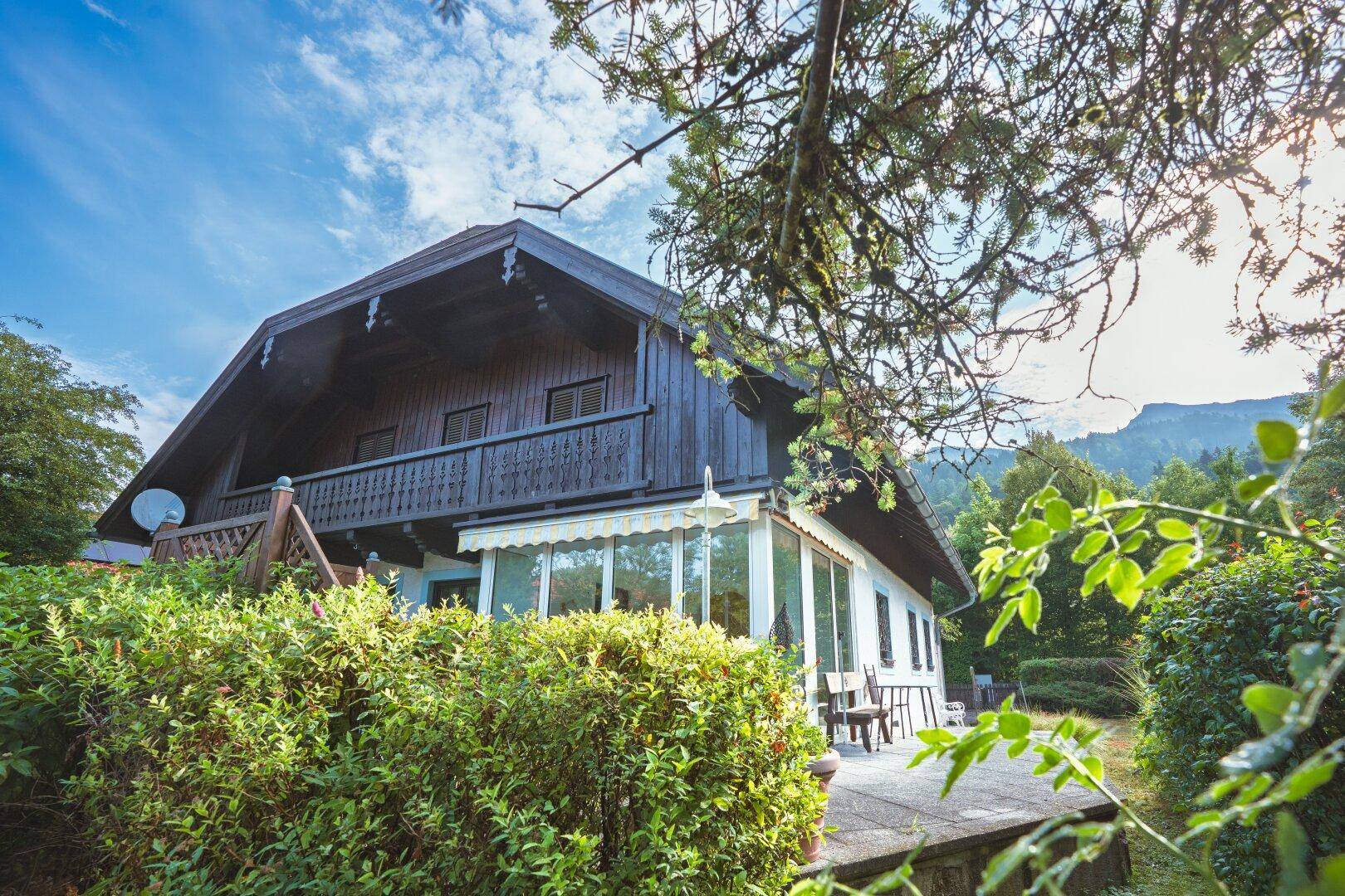 Charmantes Haus mit Wintergarten und Balkon, umgeben von üppiger grüner Vegetation.