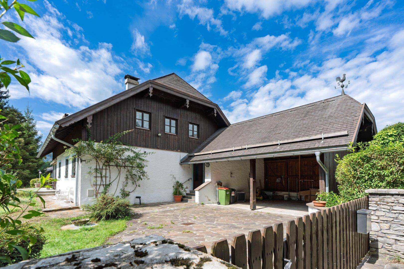 Traditionelles Haus mit Holzfassade und einem überdachten Carport im ländlichen Stil.