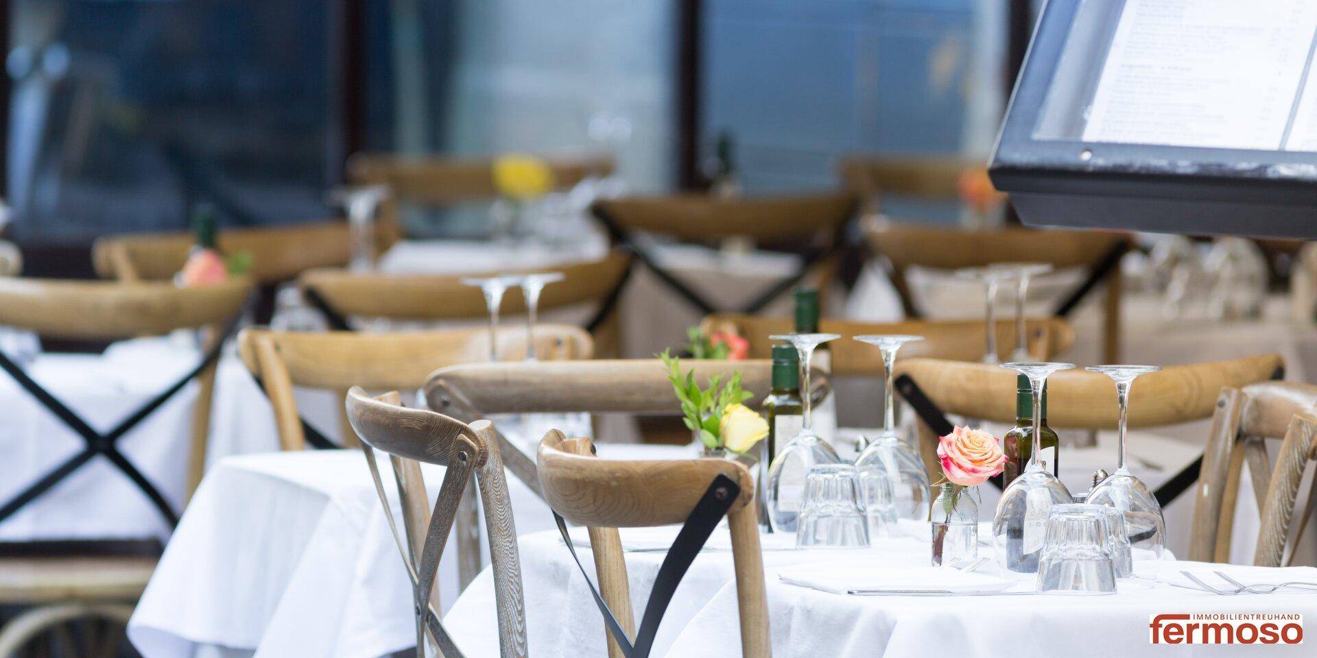Charmante Außenterrasse eines Cafés oder Restaurants mit Holztischen und weißen Tischdecken.