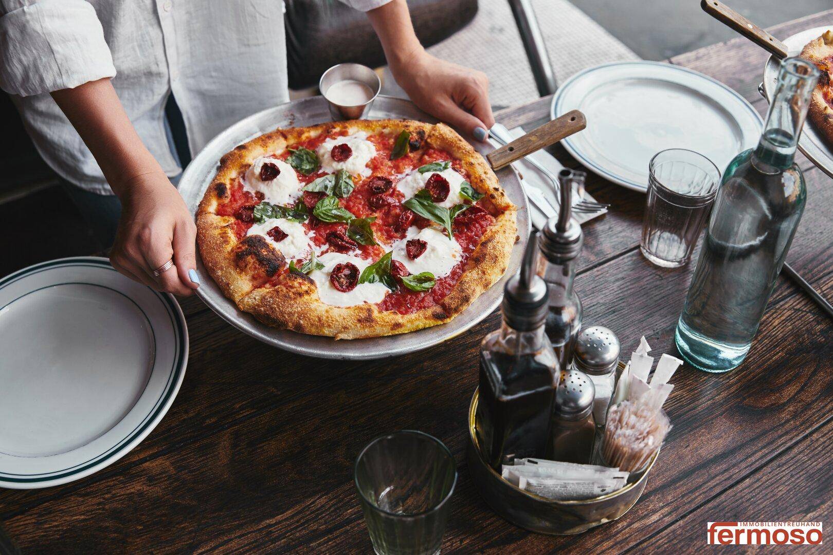 Nahaufnahme einer frisch servierten Pizza auf einem Holztisch in einem gemütlichen Restaurantambiente.