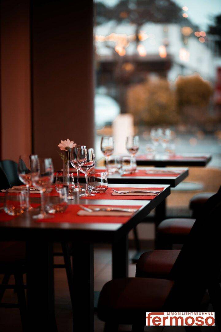 Elegantes Restaurantinterieur mit gedeckten Tischen, Weingläsern und rotem Tischläufer, bereit für Gäste.