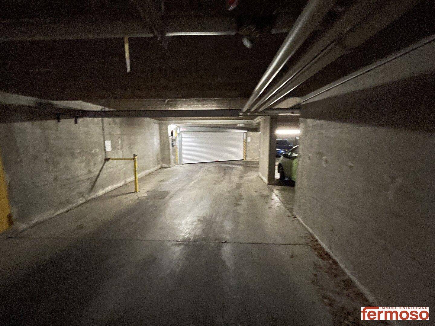 Gang in der Tiefgarage mit Betonwänden und einem Rolltor im Hintergrund.