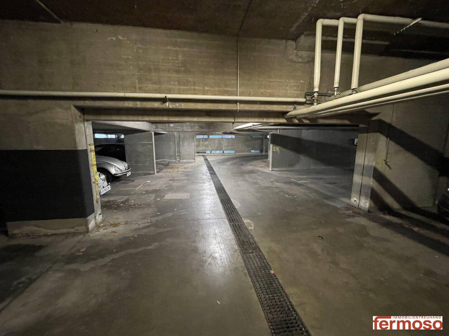Tiefgarage mit markierten Stellplätzen, Entwässerungsrinne und Betonstützen.