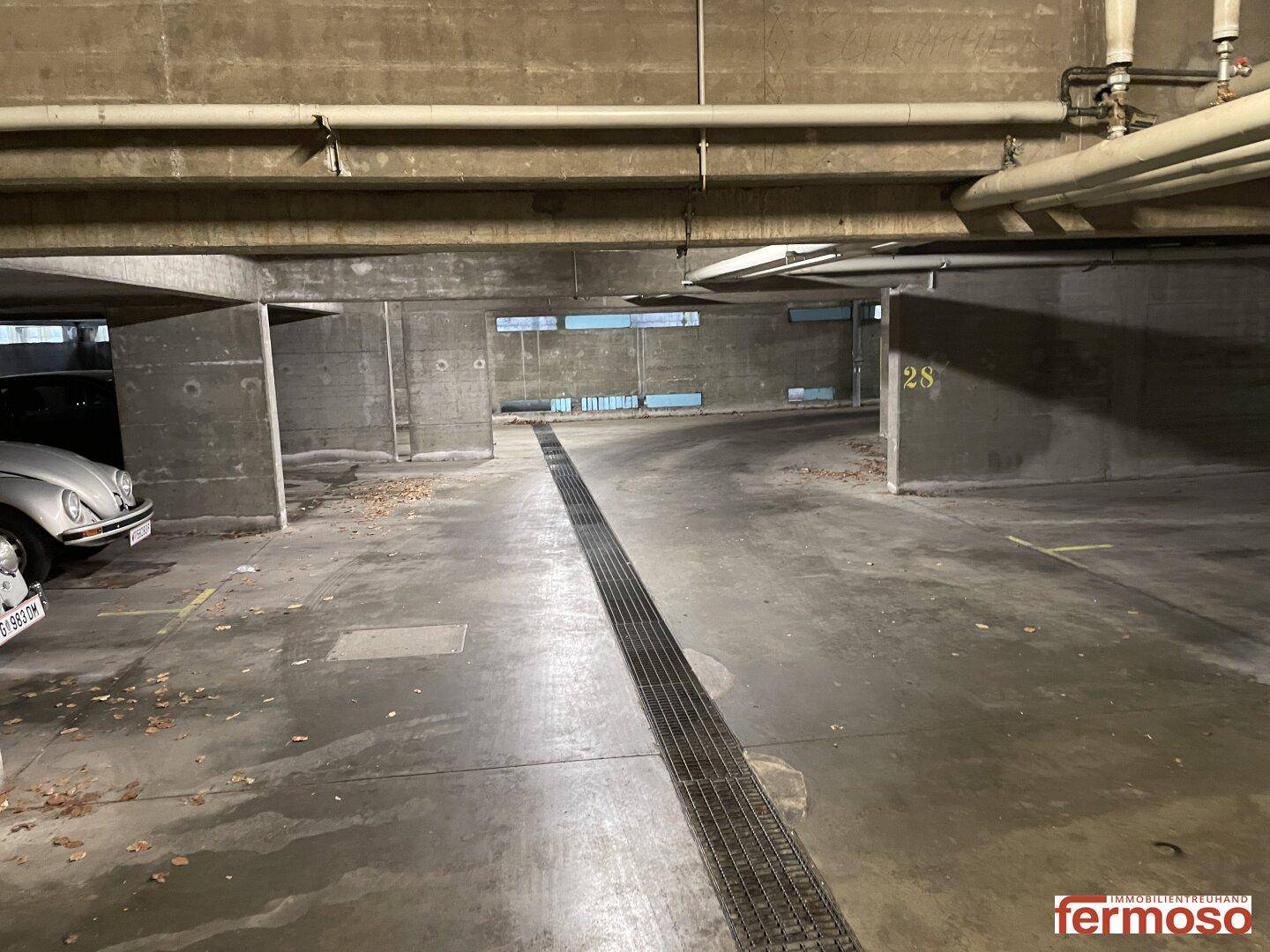 Tiefgarage mit Betonwänden, Entwässerungsrinne und einem geparkten Oldtimer.