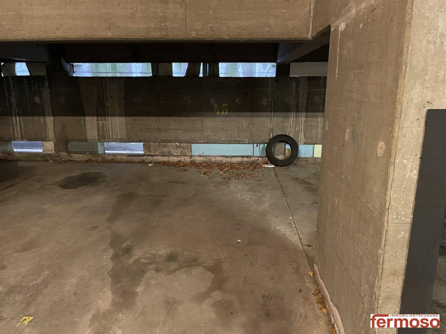 Tiefgarage mit Betonwand, kleinen Lüftungsfenstern und einem abgestellten Reifen.