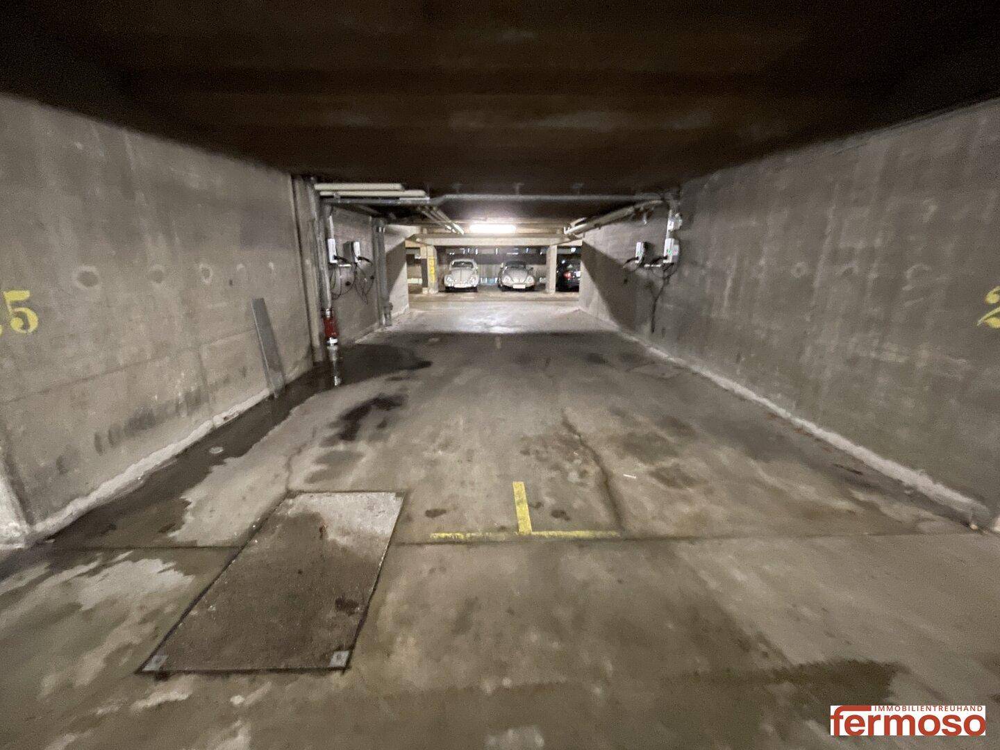 Langer Gang in der Tiefgarage mit Betonwänden und Beleuchtung im Hintergrund.