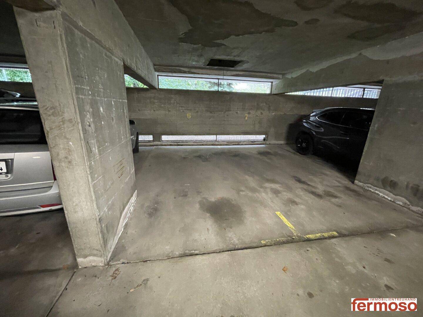 Einzelner Stellplatz in der Tiefgarage mit Betonstütze und Lüftungsfenstern.