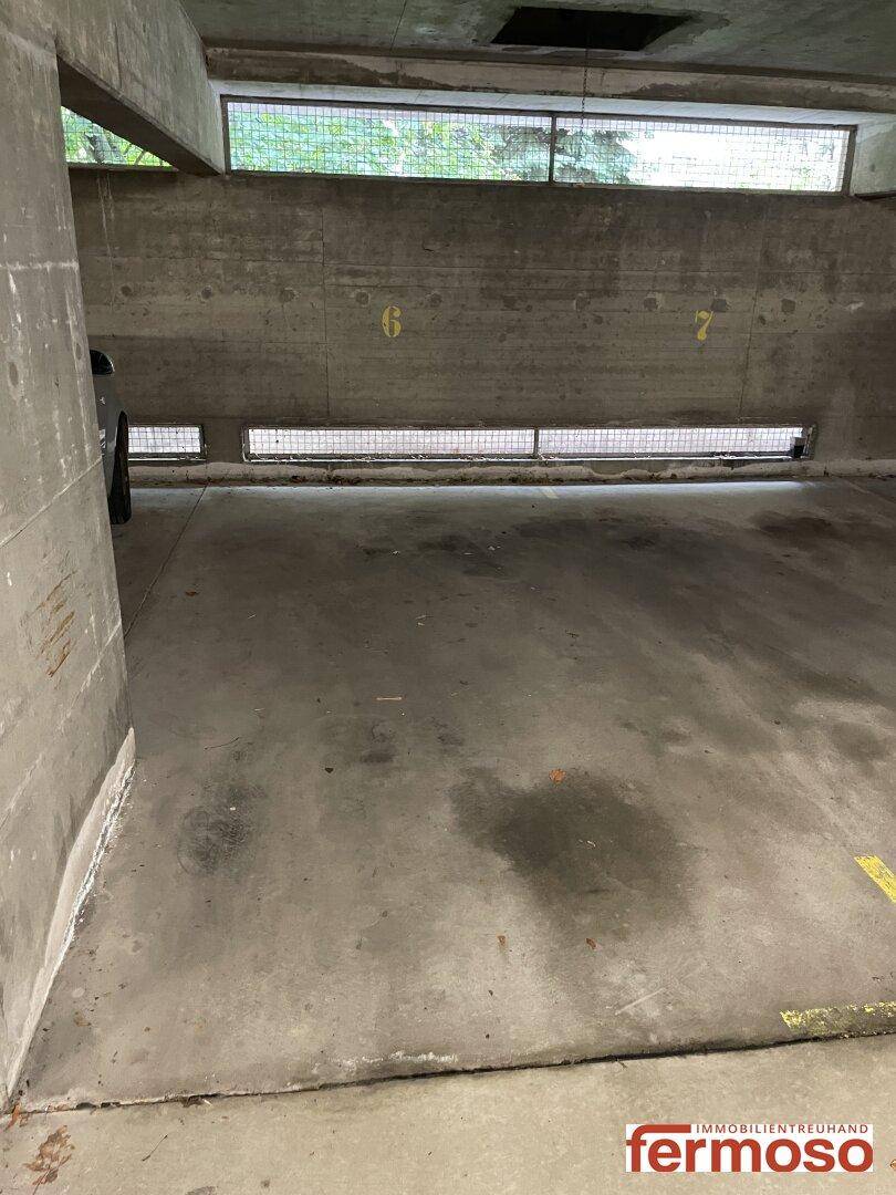 Stellplatz in der Tiefgarage mit Betonwänden und einem geparkten Fahrzeug im Hintergrund.