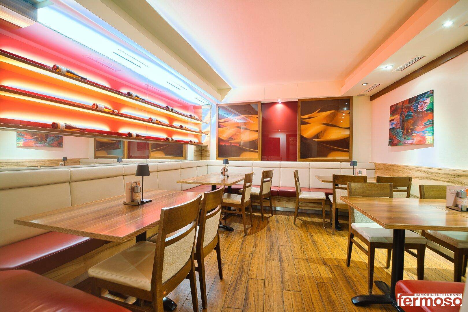Moderner Restaurantbereich mit Holzböden, gepolsterten Sitzbänken und beleuchteten Weinregalen.