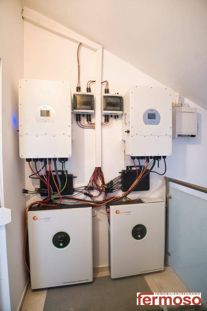 Technikraum mit mehreren Photovoltaik-Wechselrichtern und Verkabelung an einer weißen Wand.