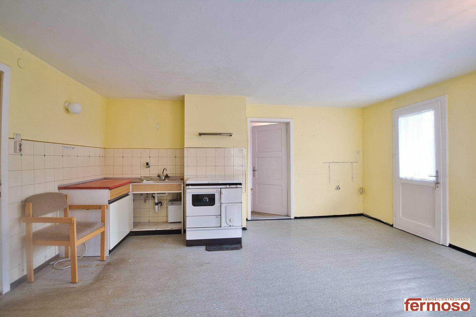 Leere Küche mit Spülbecken, traditionellem Ofen und gelben Wänden, bereit zur Renovierung.