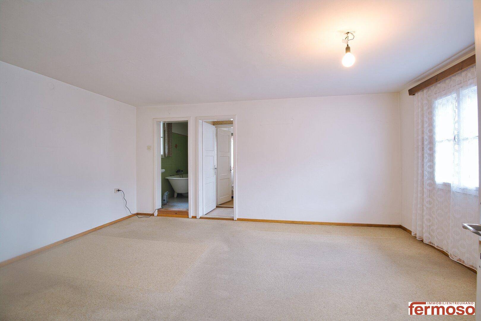 Leerer Raum mit Teppichboden und Zugang zu einem angrenzenden Badezimmer, hell und sauber.