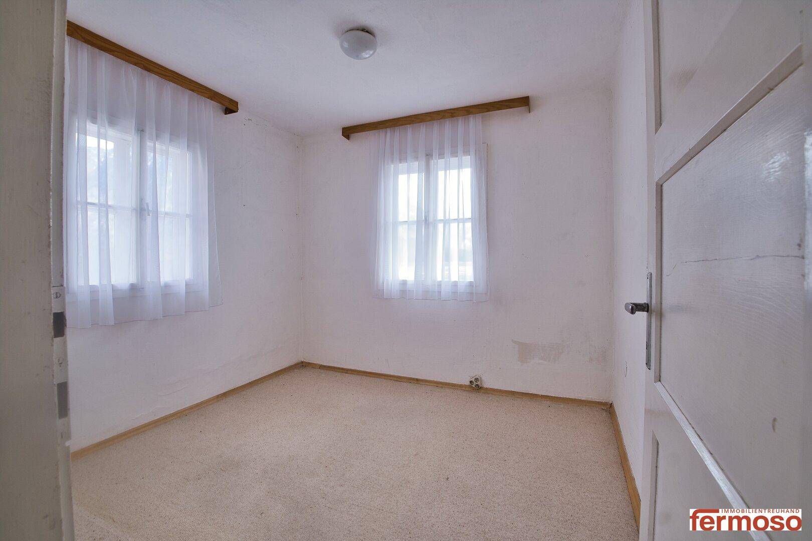 Helles, leeres Schlafzimmer mit Teppichboden und zwei Fenstern, bereit zur Einrichtung.