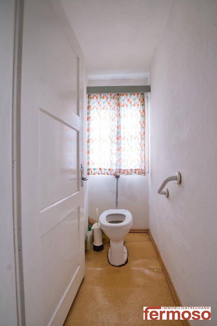 Kleines WC mit Fenster, Toilette und Haltegriff an der Wand, funktional und hell.