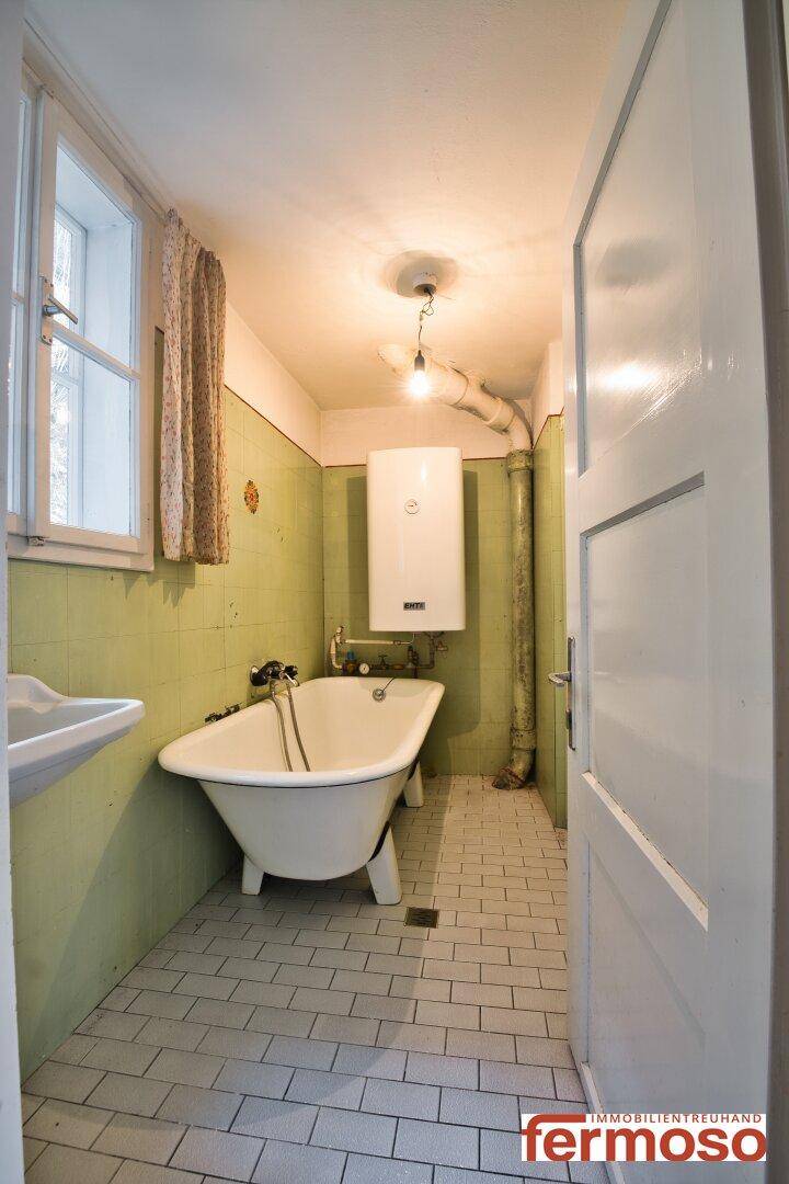 Badezimmer mit freistehender Badewanne, Fenster und grünen Wandfliesen im traditionellen Stil.