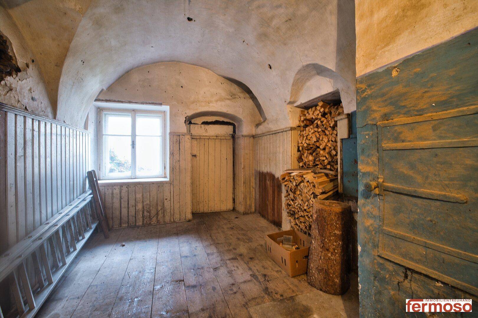 Rustikaler Lagerraum mit Gewölbedecke, Holzverkleidung und gestapeltem Brennholz.