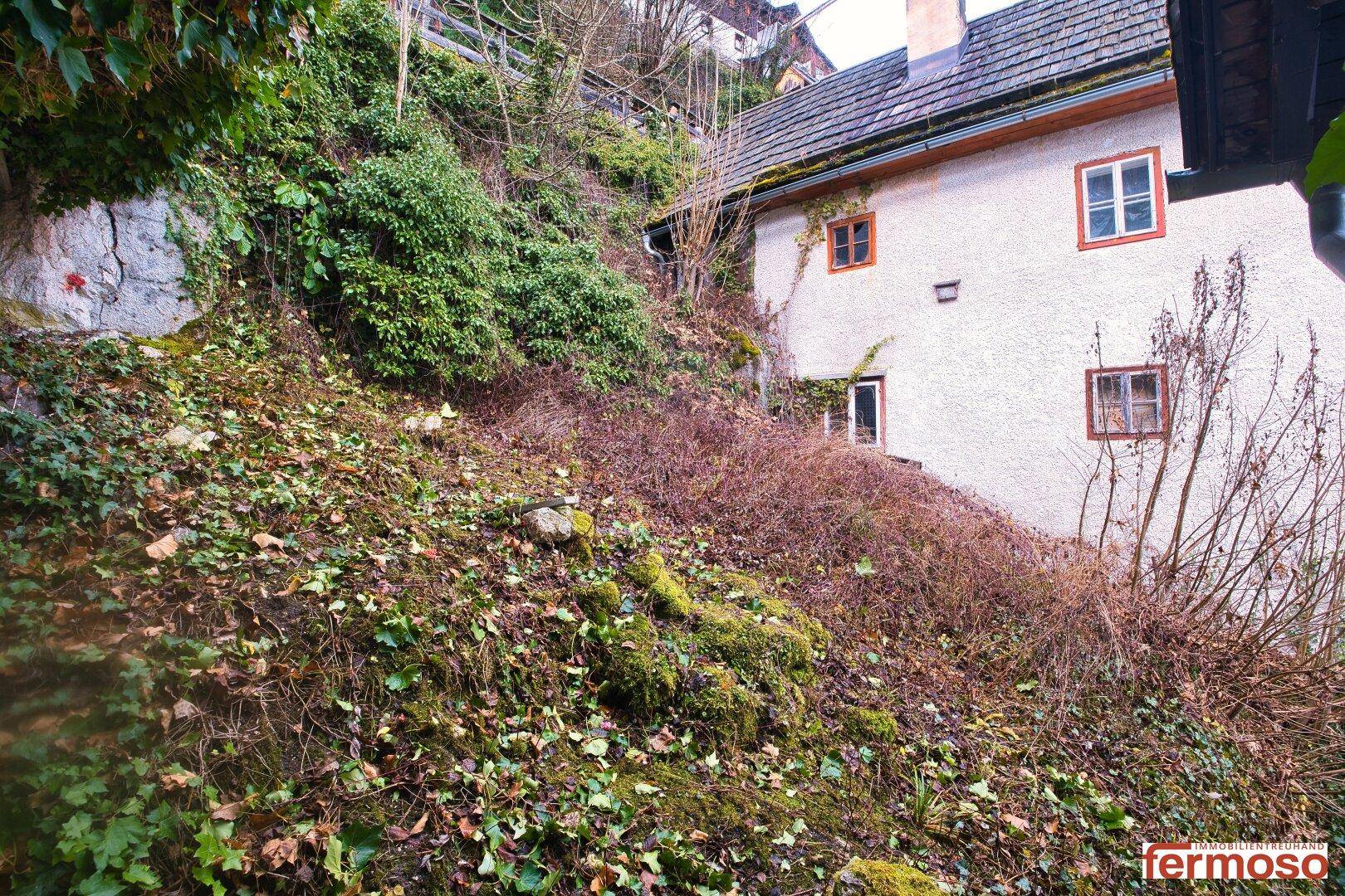 Traditionelles Haus an einem Hang mit üppiger Vegetation und alten Bäumen im Winter.