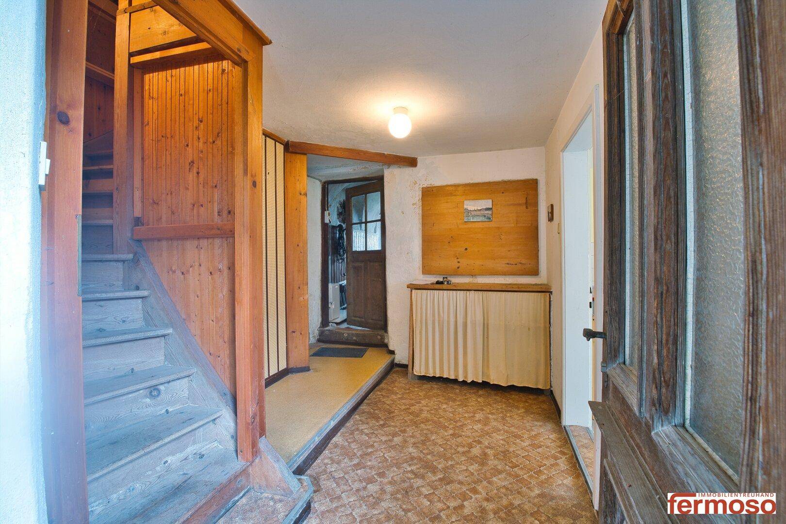 Gemütlicher Eingangsbereich mit Holztreppe, Fliesenboden und traditionellem Teppichläufer.