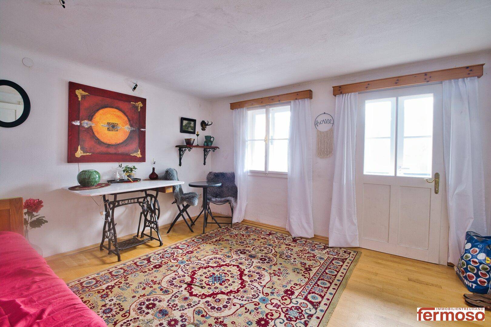 Helles Wohnzimmer mit Holzboden, rotem Sofa und Zugang zum Außenbereich durch eine Tür.