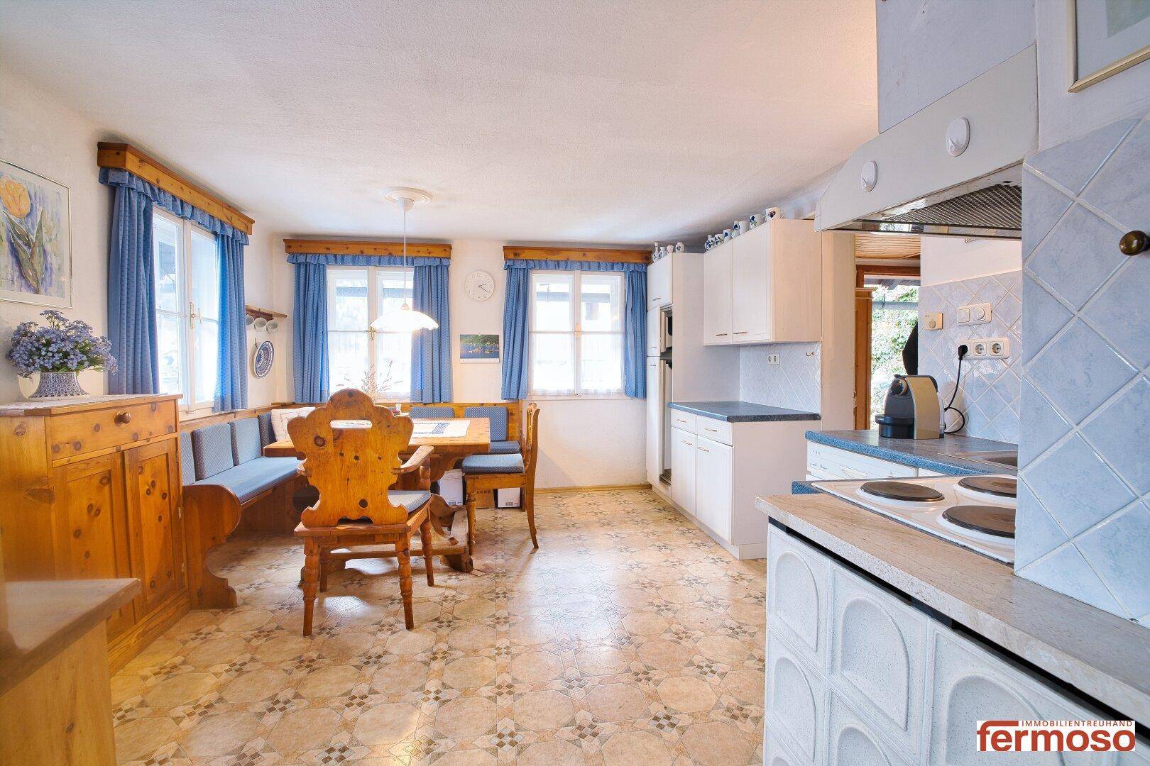 Traditionelle Wohnküche mit Holztisch, Eckbank und blauen Vorhängen, gemütlich eingerichtet.