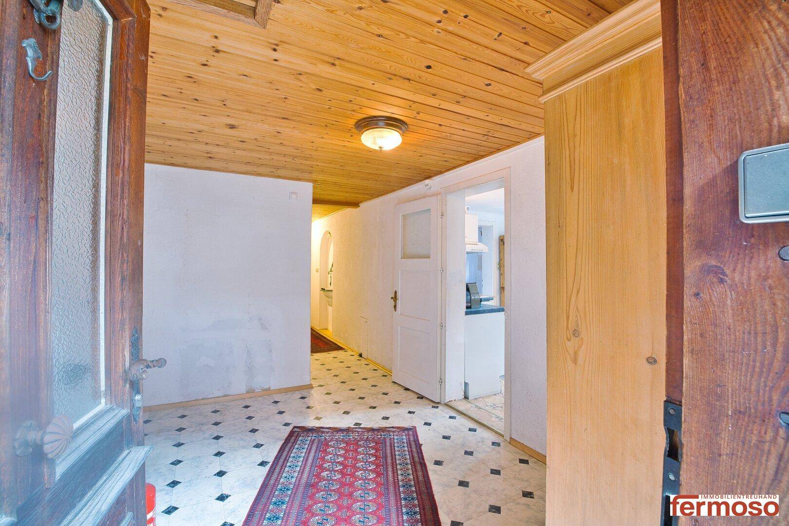 Heller Eingangsbereich mit Holzdecke, Fliesenboden und traditionellem Teppichläufer.