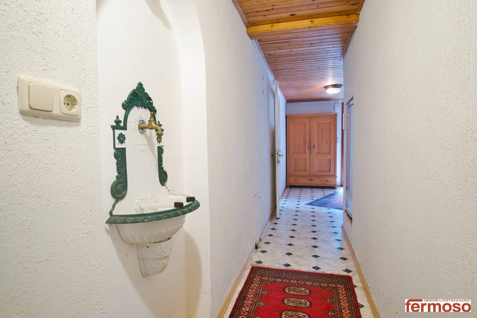 Schmaler Flur mit Holzdecke, Fliesenboden und einem dekorativen Wandbrunnen im traditionellen Stil.