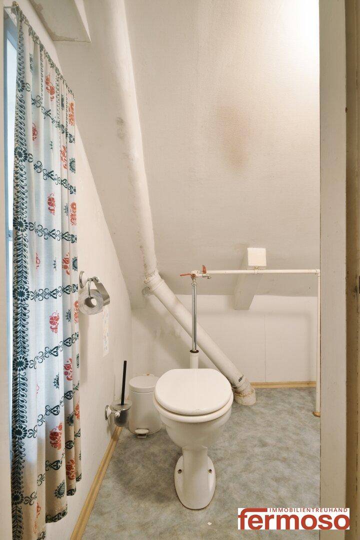 Dachgeschoss-WC mit schrägen Wänden, Fenster und einfacher Ausstattung, funktional und hell.