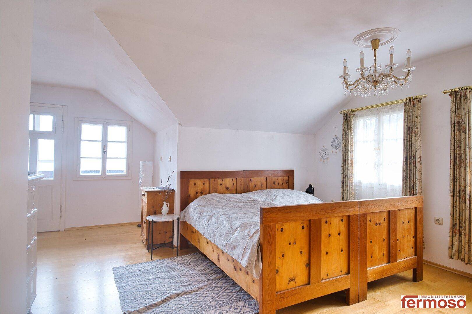 Helles Schlafzimmer mit Holzbett, Dachschräge und Kronleuchter, bietet eine gemütliche Atmosphäre.