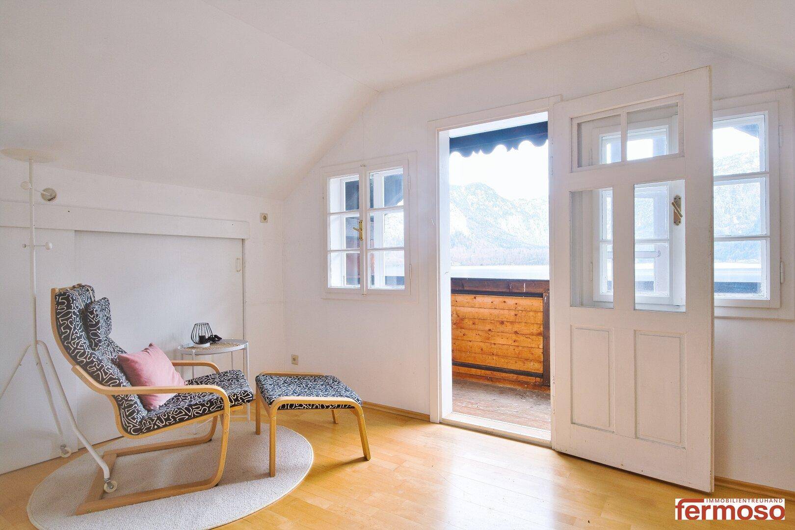 Heller Wohnbereich mit bequemen Sessel und Zugang zu einem Balkon mit Bergblick.