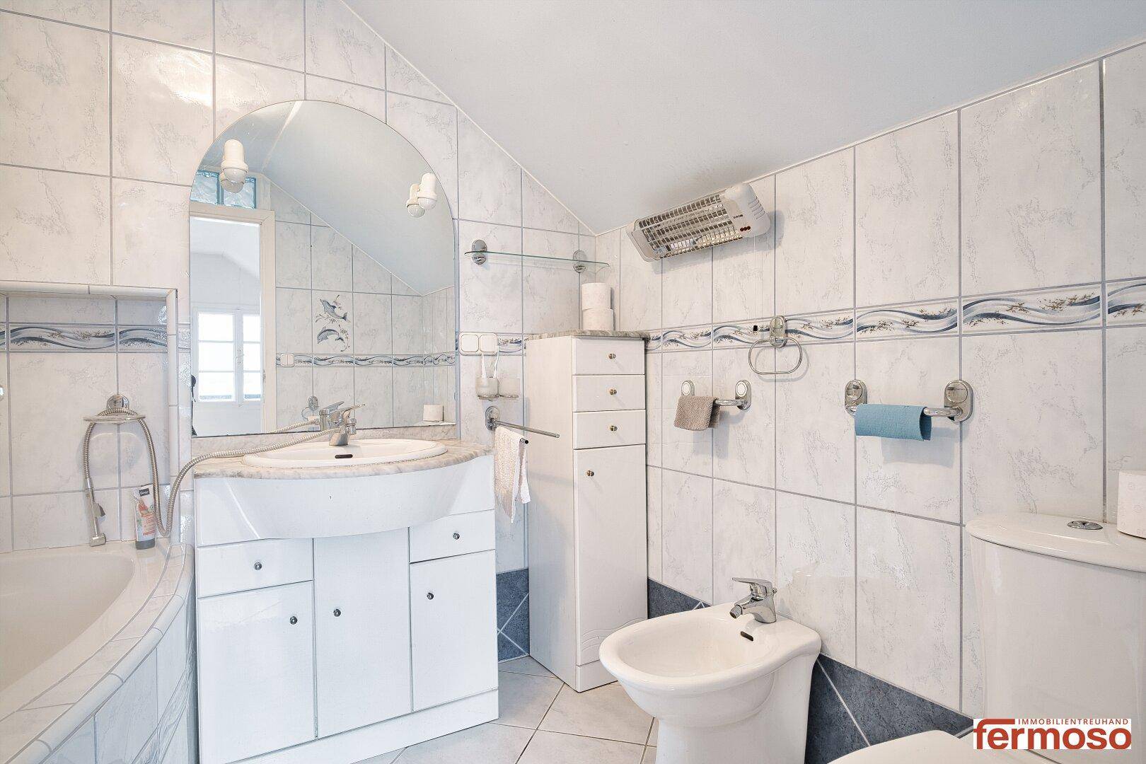 Gefliestes Badezimmer mit Eckbadewanne, Bidet und Waschbecken, ausgestattet mit Wandheizung.