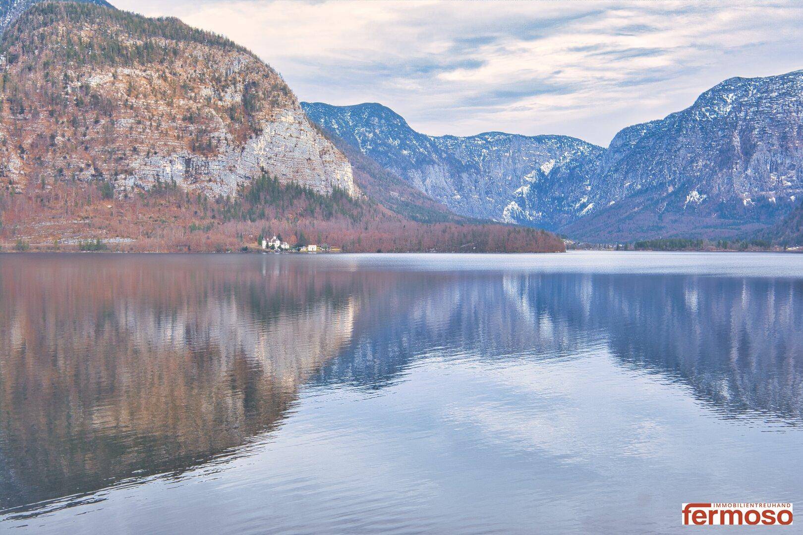 Malerischer Blick auf einen ruhigen See, umgeben von majestätischen Bergen unter bewölktem Himmel.