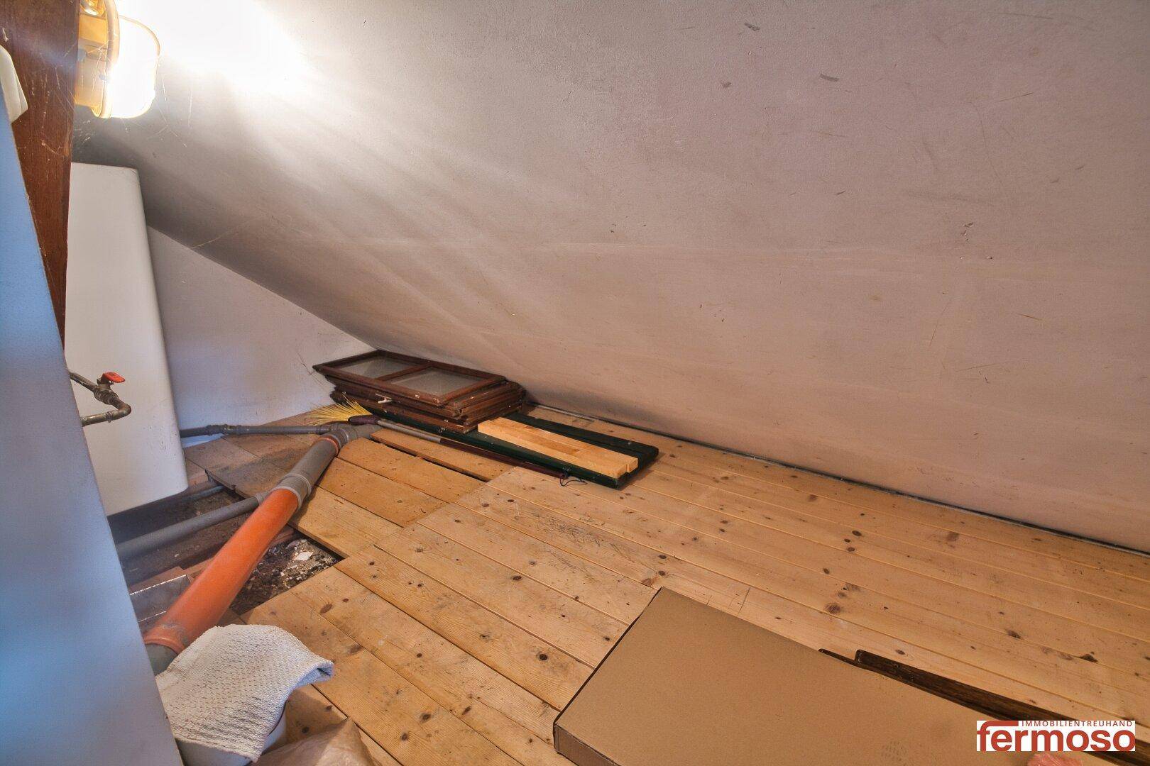 Dachbodenbereich mit sichtbaren Holzplanken und Dachschräge, der Renovierungsbedarf zeigt.