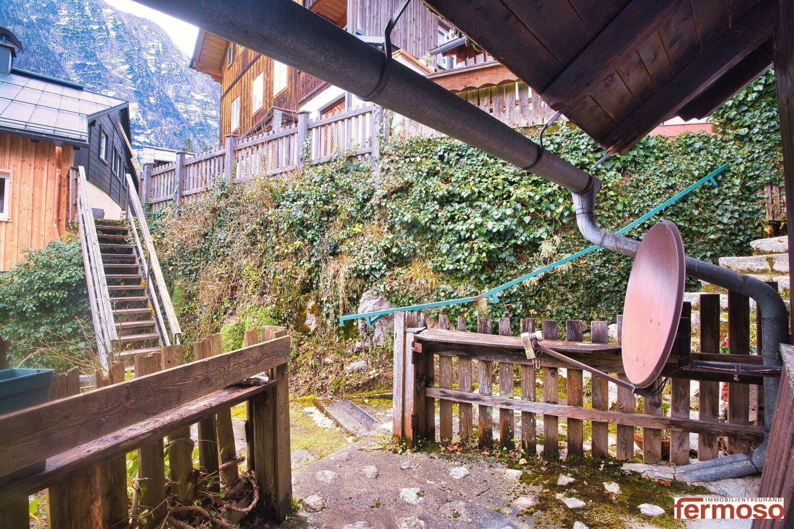 Traditionelles Holzhaus mit Steintreppe und üppigem Efeu, eingebettet in die bergige Landschaft.