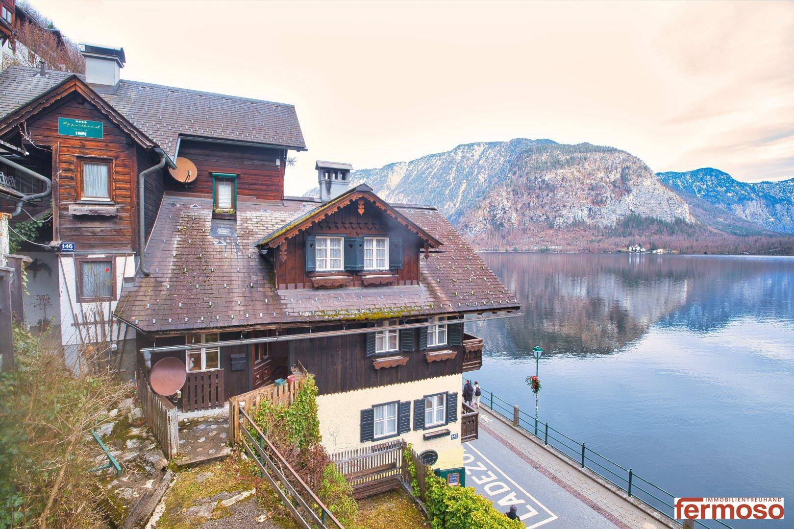 Panoramablick auf ein traditionelles Holzhaus am See, umgeben von einer beeindruckenden Bergkulisse.