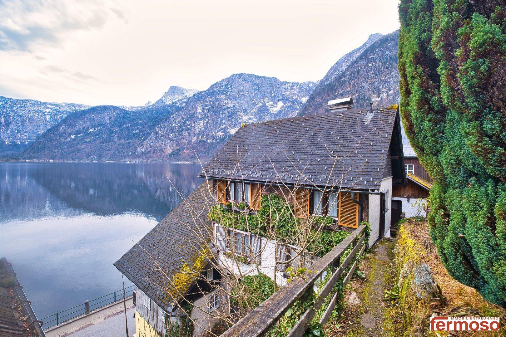 Traditionelles Haus mit dunklem Dach, idyllisch am Hang gelegen mit Blick auf See und Berge.