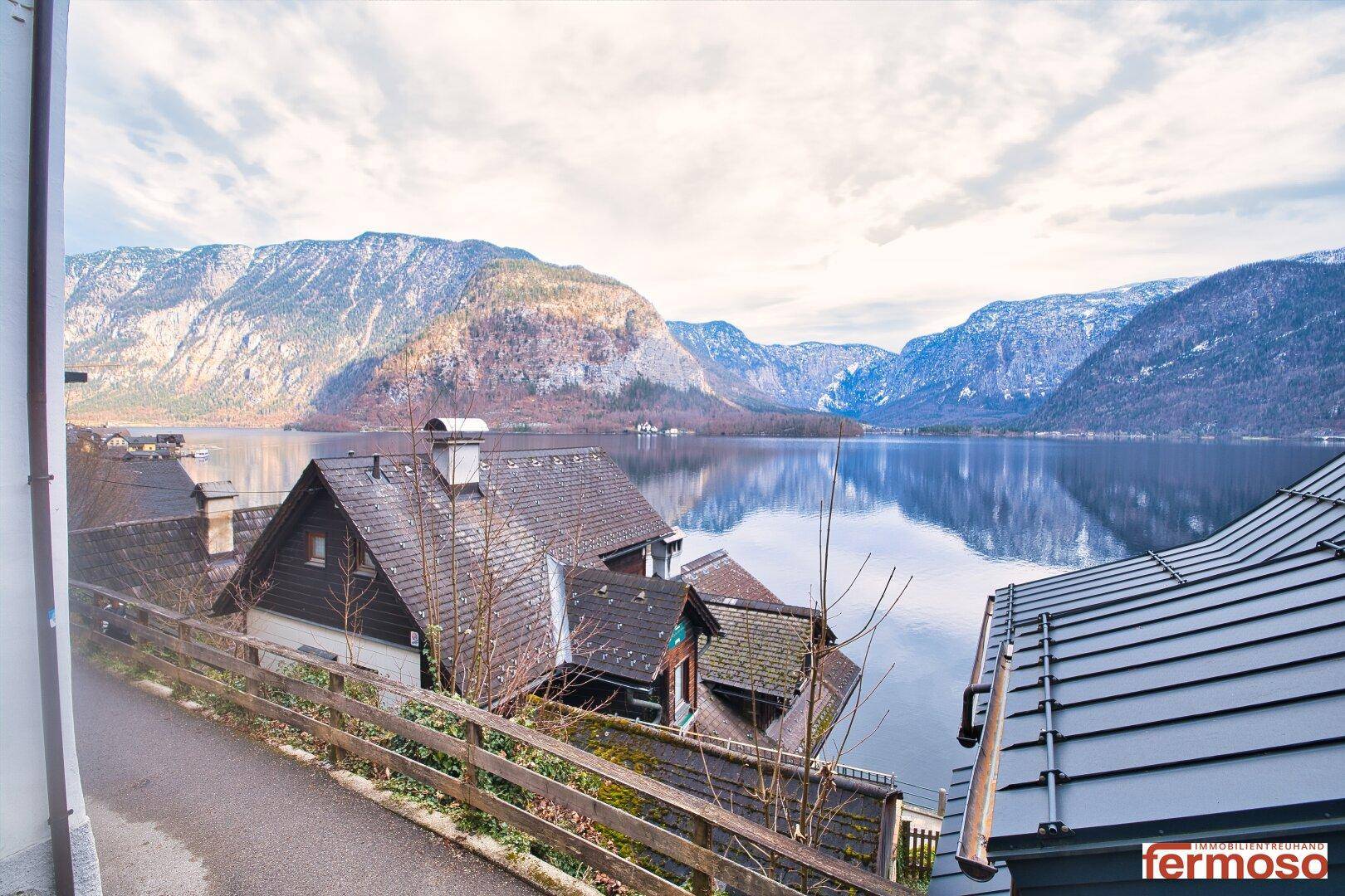 Mehrere traditionelle Häuser mit dunklen Dächern, die einen weiten Blick auf den See und die Berge bieten.